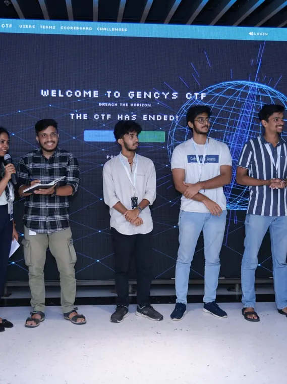 Event participants stand together on a stage beneath a GenCys display.