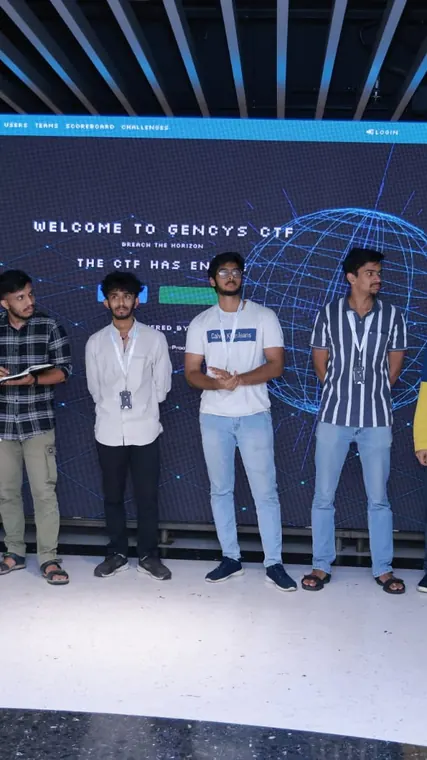 Three participants pose on stage at a GenCys event.