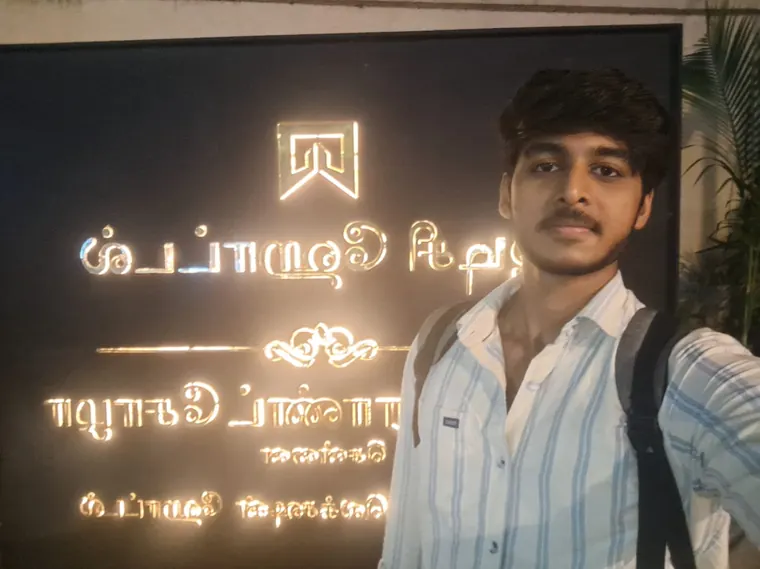 A person stands beside an illuminated Tamil sign.